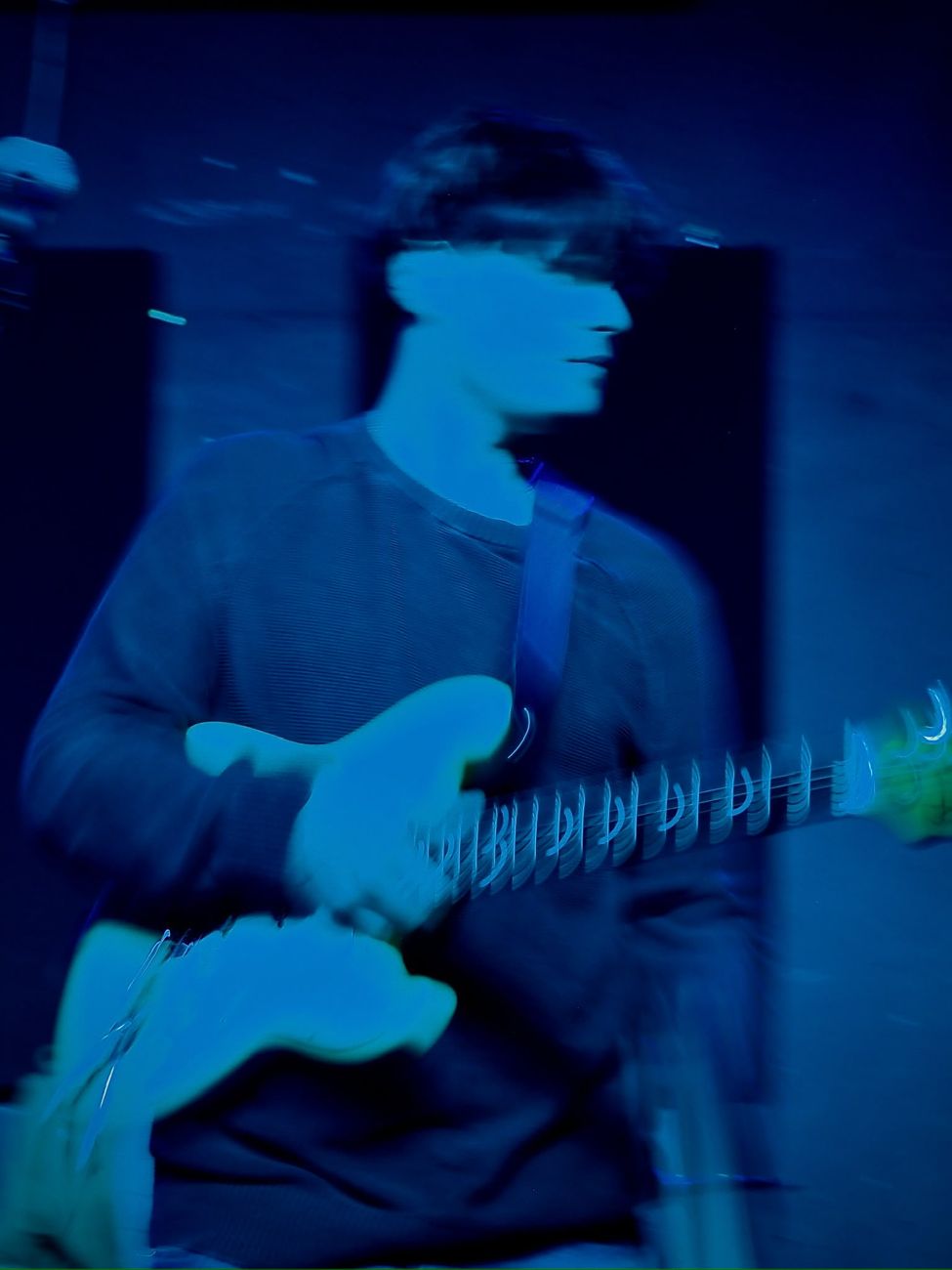 Ben playing guitar under blue stage light, in motion blur