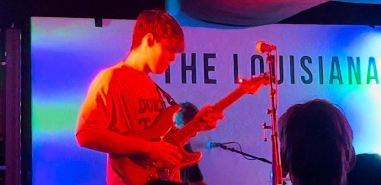 Ben playing guitar under red light in front of The Louisiana sign on stage