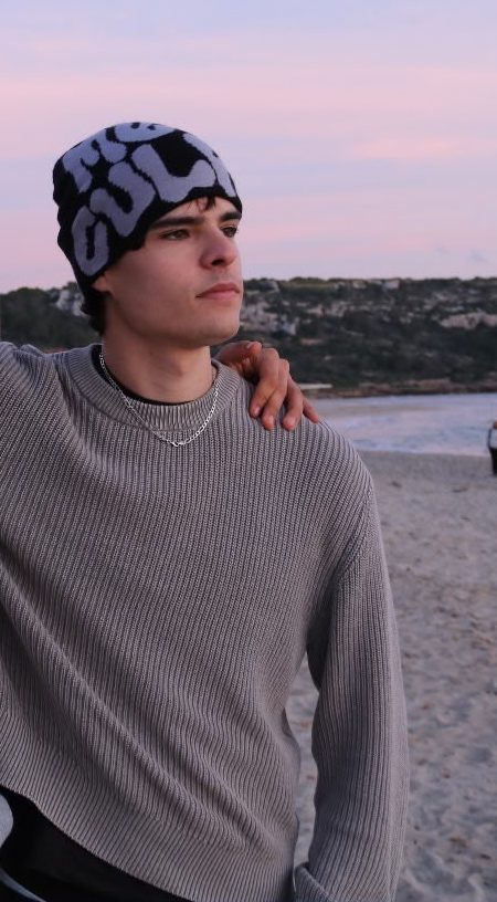 Ben in a patterned beanie on a Menorca beach at dusk